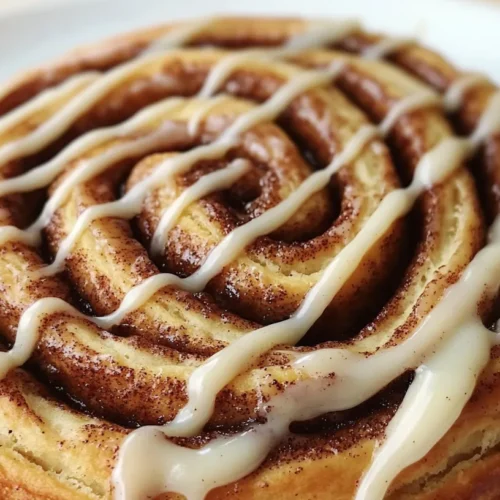 Close-up of a warm, freshly baked cinnamon roll with vanilla icing melting over its golden brown swirls, served on a white plate.