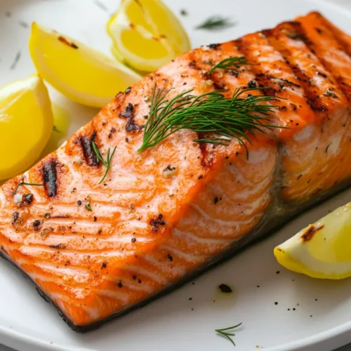 Close up view of a Traeger grilled salmon fillet with crispy skin and lemon garnish on a white plate.