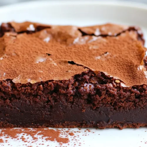 A close-up of a single serving of low fat protein oat brownies on a white plate, featuring a fudgy texture, cracked top, and a drizzle of dark chocolate.