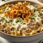 Close-up of creamy French onion beef and noodles in a ceramic bowl with melted cheese and crispy onions